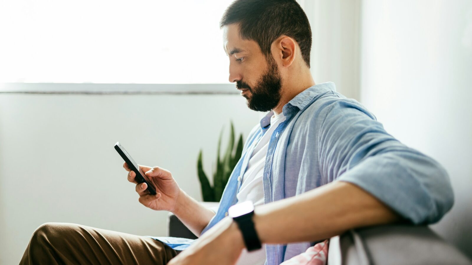 A man sitting on a couch reading his text messages on his phone, representing DIY separation agreement made via text message in Alberta