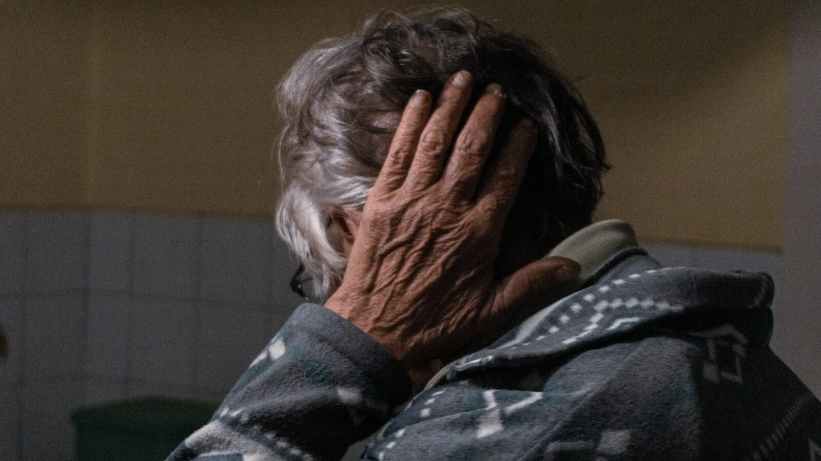 An elderly woman with her hand pressed to the side of her head, representing elder abuse.