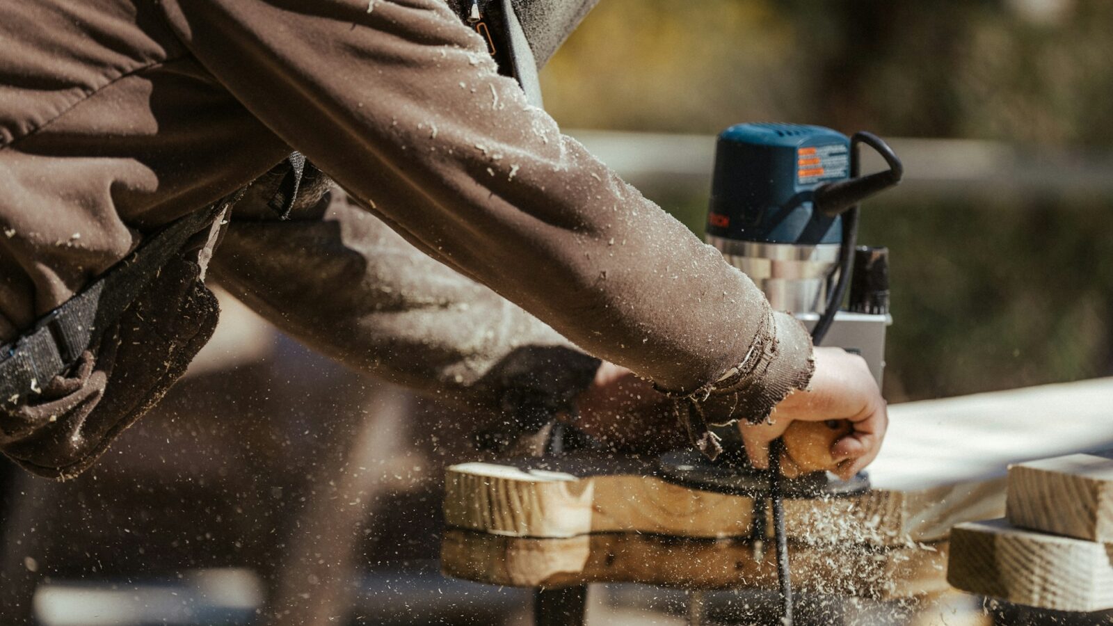 A contractor is bent over a plank of wood and sanding it while sawdust fills the air around him, representing a contractor walking off the job.