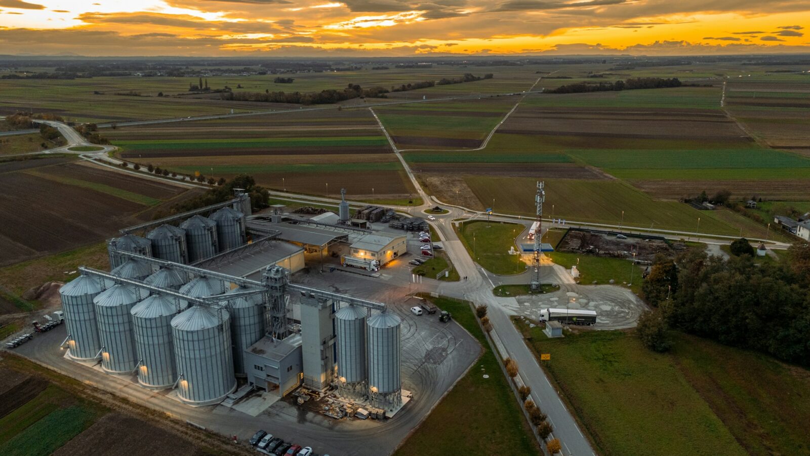 Grain silos surrounded by green and brown fields with the setting sun seeping through gaps in gray clouds, representing injunctions and trade secrets.