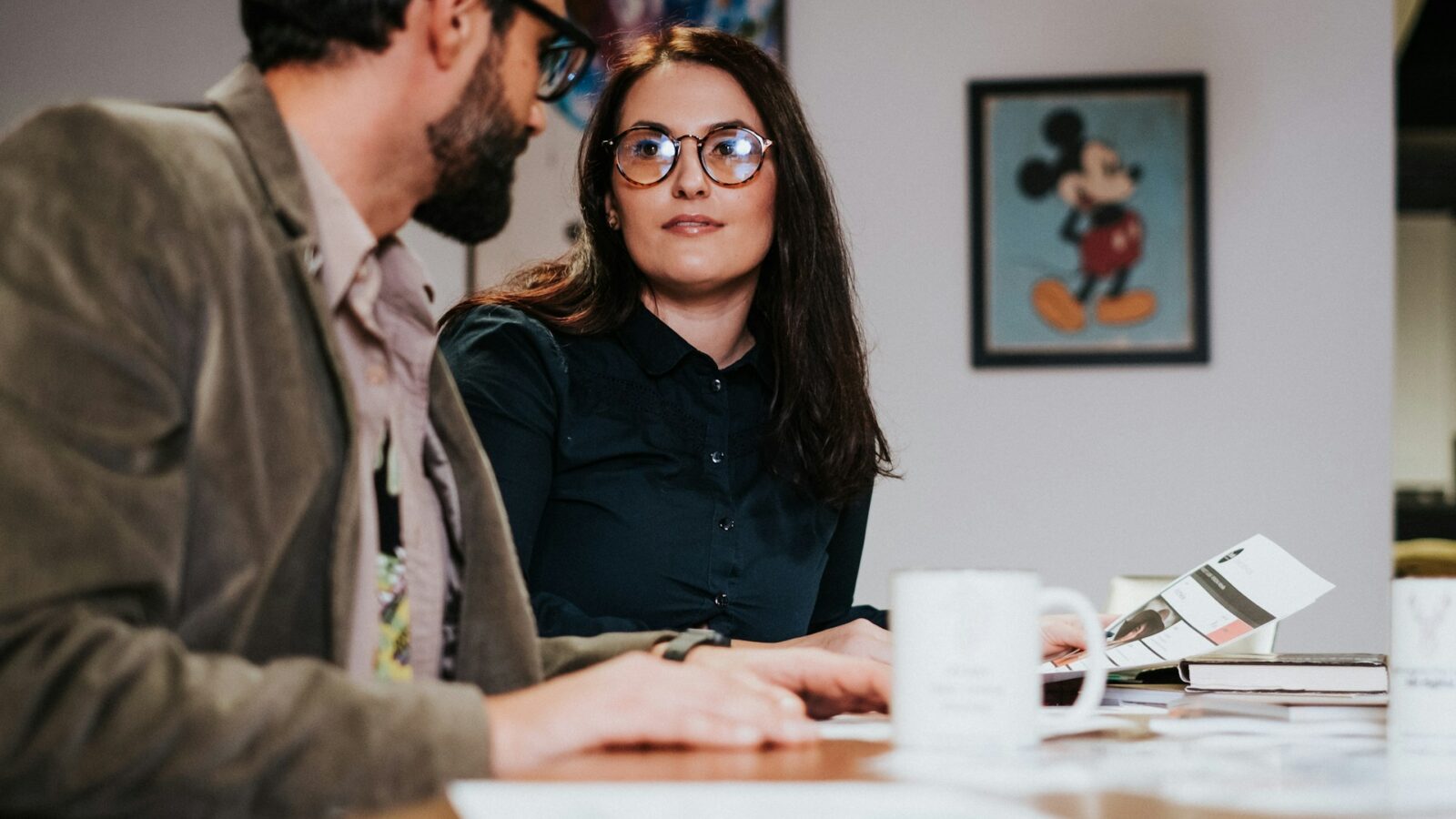 A divorcing husband and wife sit next to each other at a board table in their ofice reviewing their company's documents, representing divorce and Alberta business owners.
