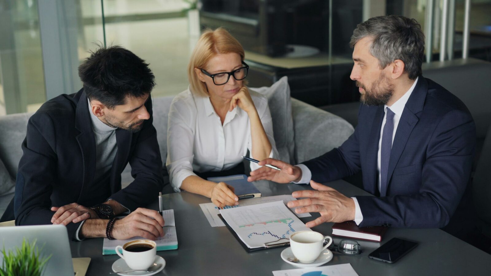 Two businessmen and a businesswoman review documents at a board table, representing business succession planning in Alberta.