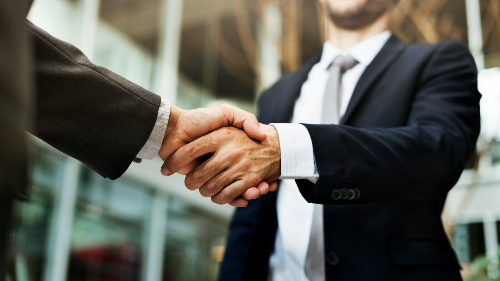 Two businessmen, shown from the chin down, shake hands in an office building, representing silent partners in Alberta.