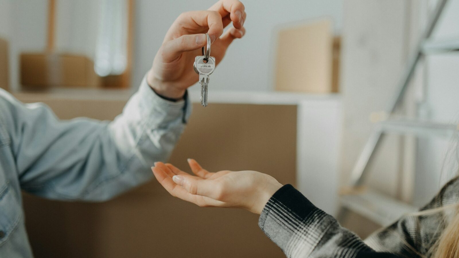 A man's arm is streetched out, his hand holding a set of house keys ready to drop into the waiting hand cupped beneath is, representing remedies for breach of real estate contract.