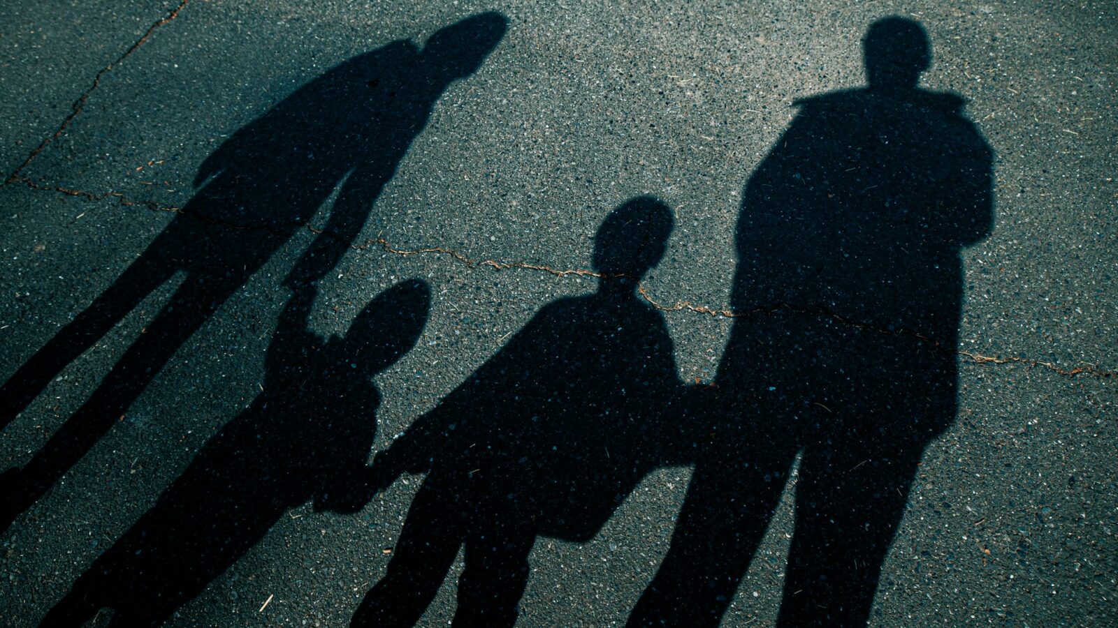 Shadows of a man and woman holding the hands of their children silhouetted against cracked pavement, representing shared parenting and child support.