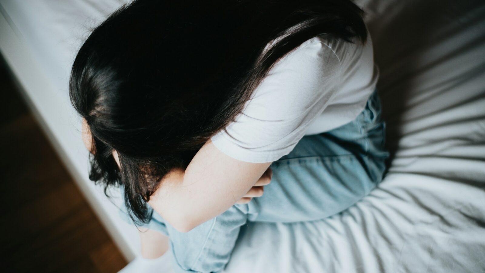 A woman with her head in her arms, sitting on the edge of a bed, representing mental health leave and discrimination accommodation in Alberta workplaces.