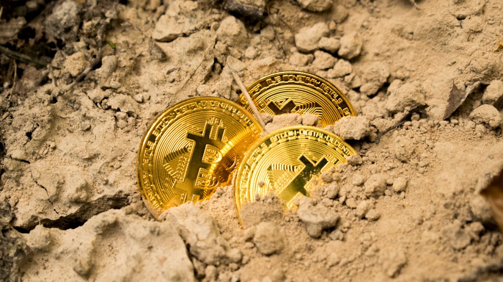Three golden bitcoins partially buried under a pile of dirt, representing Alberta surface rights and bitcoin.