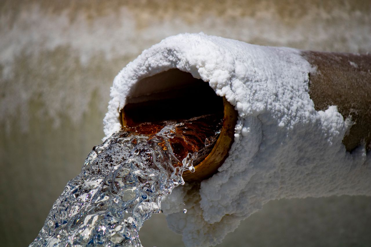Close-up of water flowing out of an ice and snow-covered industrial pipe, representing occupational health and safety in Alberta.