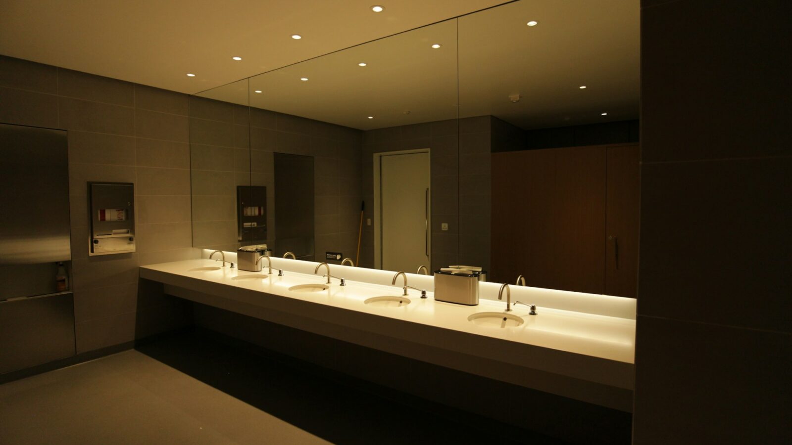 A row of sinks in front of a wall of mirrors in a public workplace bathroom, representing Alberta Tort of Intrusion Upon Seclusion.